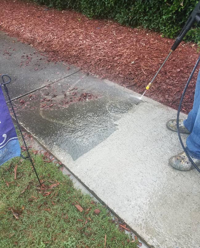 a sidewalk being pressure washed, showing a super grimy dirty side and a side that's already been cleaned and looking noticeably much better