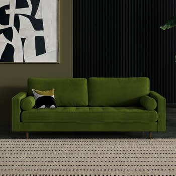 Green velvet sofa with a black and white pillow, in a room with abstract art and a rug. Perfect for modern home decor shopping