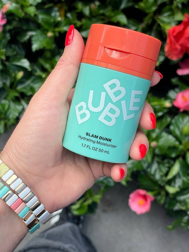 Person holding Bubble Slam Dunk Hydrating Moisturizer with a floral background
