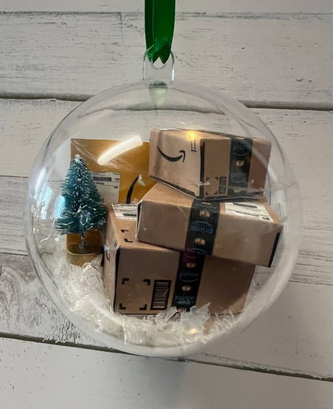an ornament with a tiny tree and mini amazon packages inside 