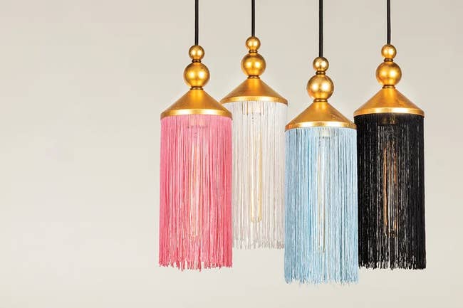 Three pendant lights with fringed lampshades in pink, white, and black, hanging in a line