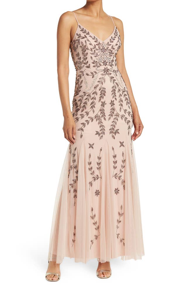 A model wears an elegant, sleeveless gown embellished with floral embroidery, suitable for formal events