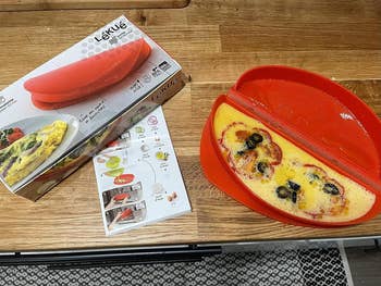 A reviewer's omelet maker filled with an uncooked egg, peppers, and black olives