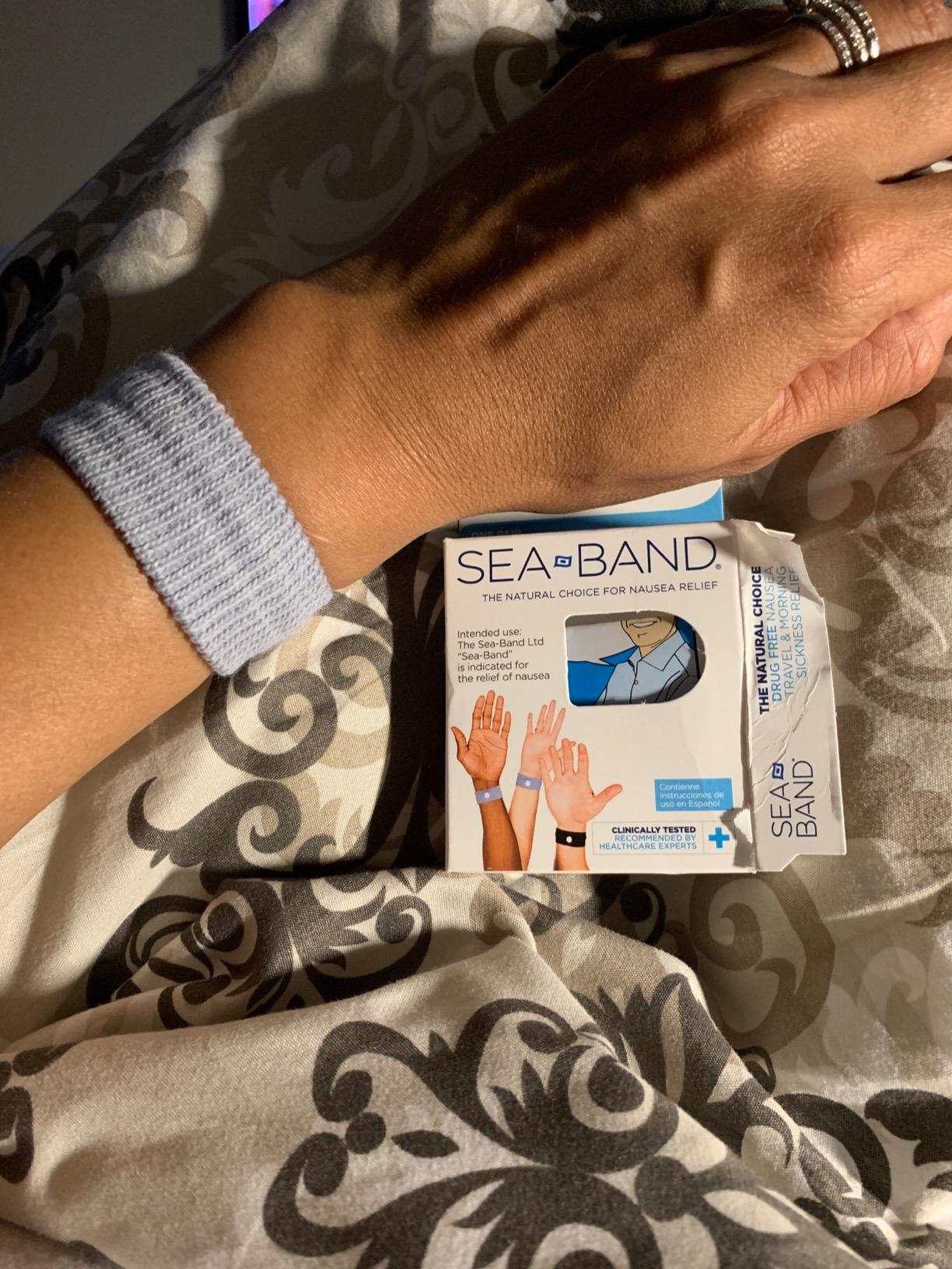 Close-up tangan yang mengenakan gelang akupresur Sea-Band di samping kotak produk Sea-Band