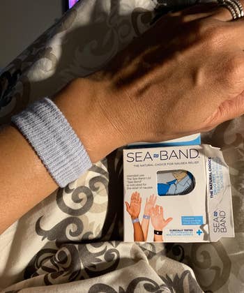 Close-up tangan yang mengenakan gelang akupresur Sea-Band di samping kotak produk Sea-Band