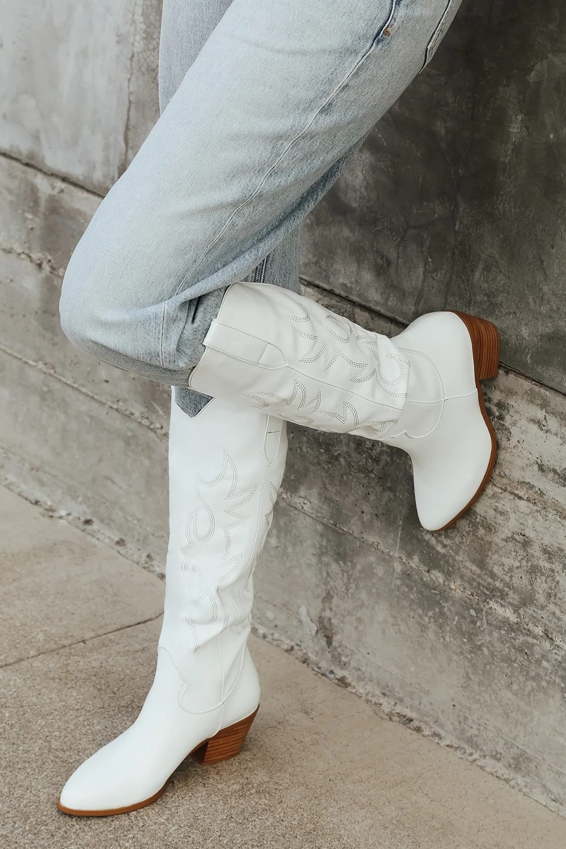 Model wearing knee high white cowboy boots with wooden heel on pavement