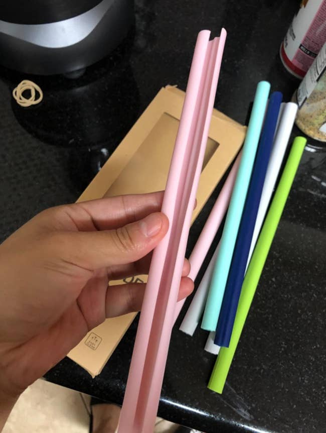 Reviewer with a set of multicolored straws holding a pink one open horizontally showing inside 