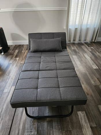 A modern, grey, tufted daybed with a matching pillow is displayed successful  a stylish country   with woody  floors