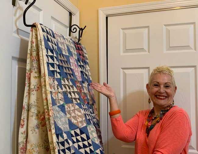 A model pointing towards the hanger on the back of a door with a quilt
