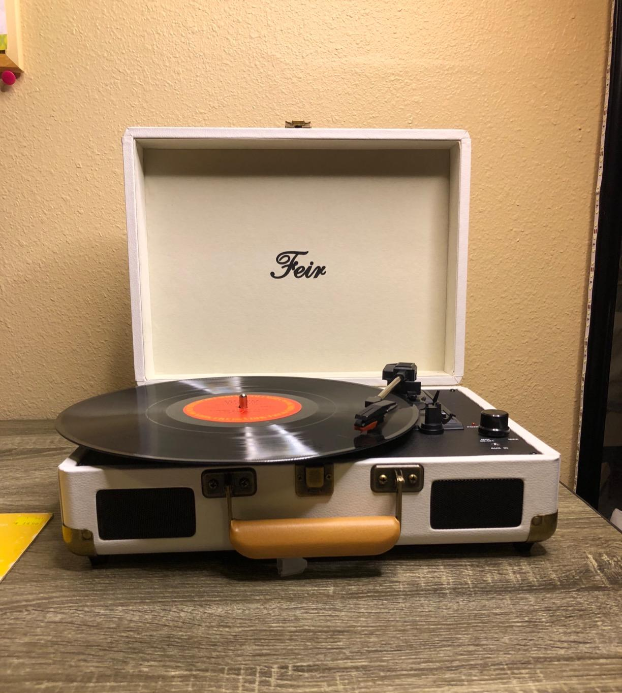 Reviewer image of white suitcase turntable with silver and black stylus on record sitting on dark wooden table