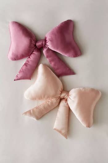 Four satin decorative knot pillows in soft pink shades arranged artistically on a neutral background