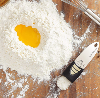 the measuring spoon filled with salt next to a pile of flour and a whisk