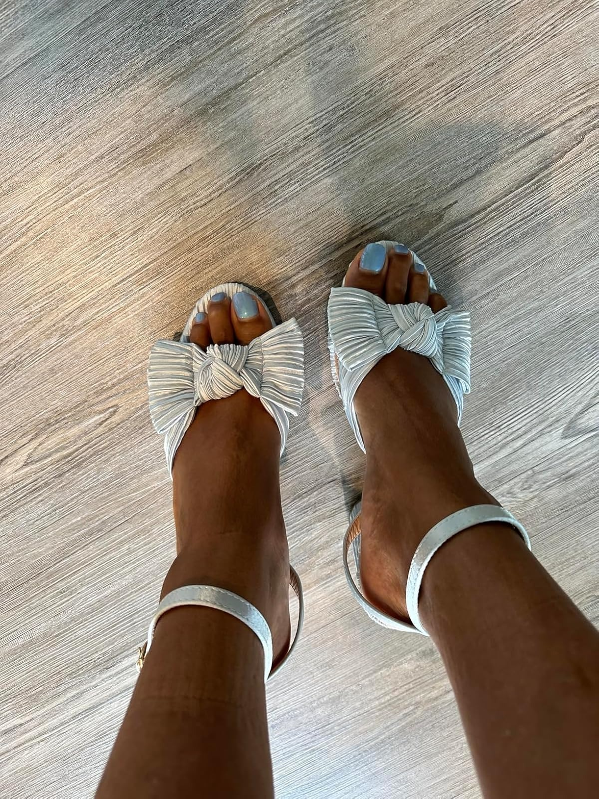 Stylish strappy sandals with ample  bows connected  toes, worn connected  a woody  floor