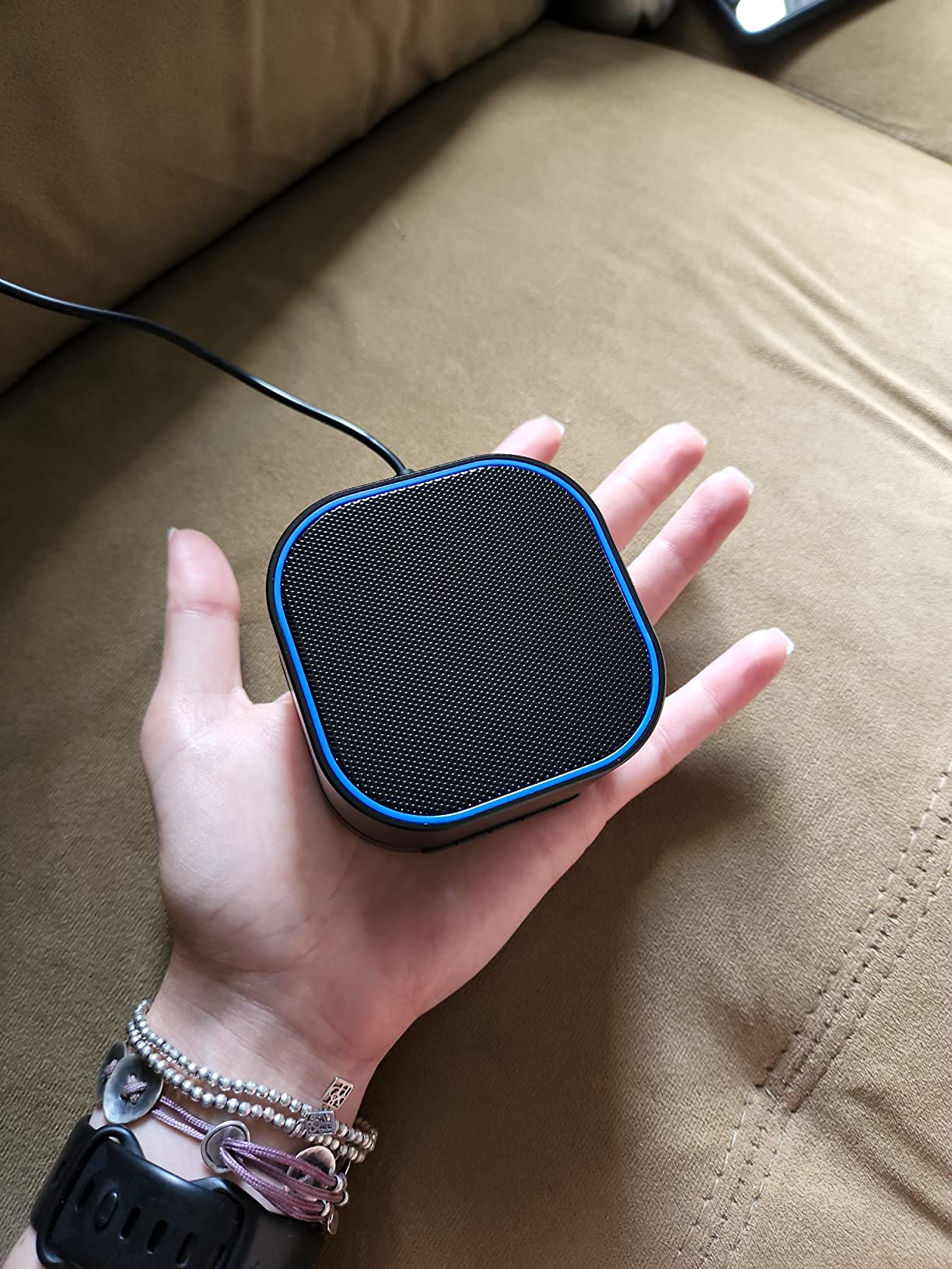 Hand holding a compact, quadrate  wireless talker  connected  a sofa, showcasing its tiny  size and portability
