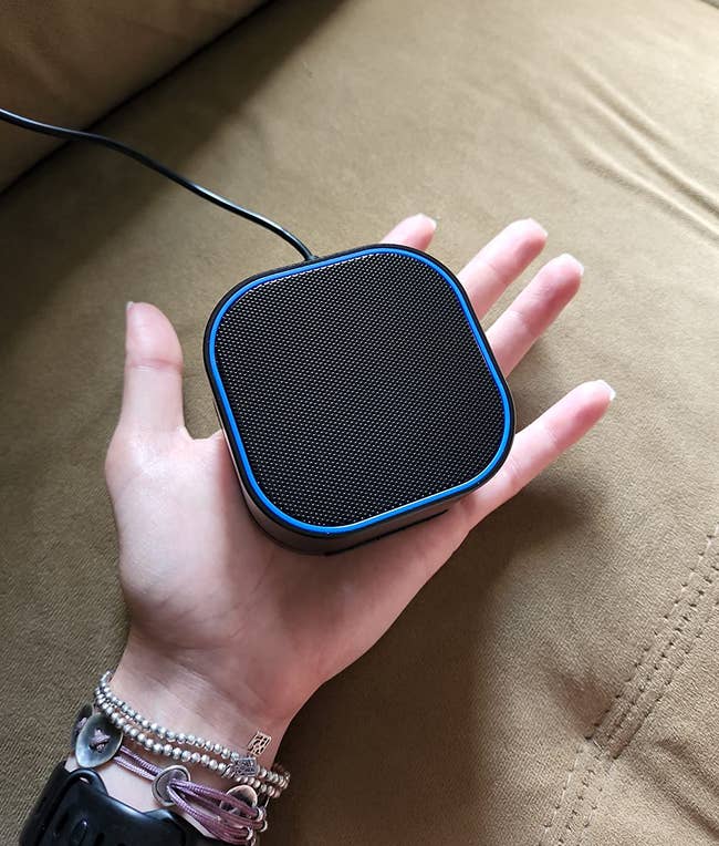Hand holding a compact, quadrate wireless talker connected a sofa, showcasing its tiny size and portability