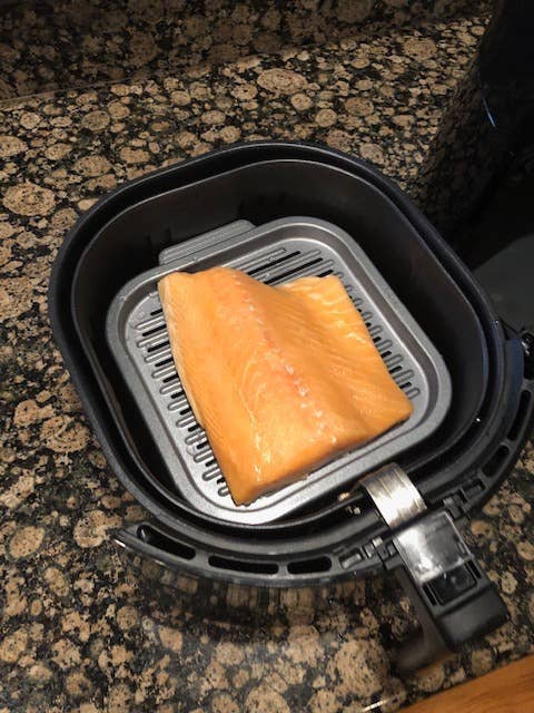 Raw salmon sitting on a grill plate in an air fryer basket