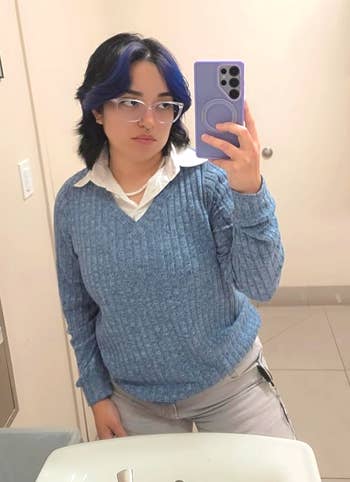 Person successful  casual, cozy bluish  sweater and achromatic  collared garment  taking a reflector  selfie successful  a bathroom