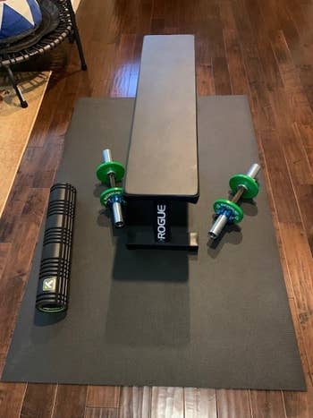 same exercise mat under weight lifting bench and green adjustable weights on floor