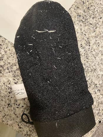reviewer showing the scrub mitt with a lot of dead skin all over it