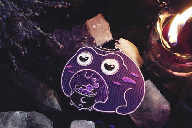 the purple frog wearing a witch hat in front of a cauldron patch