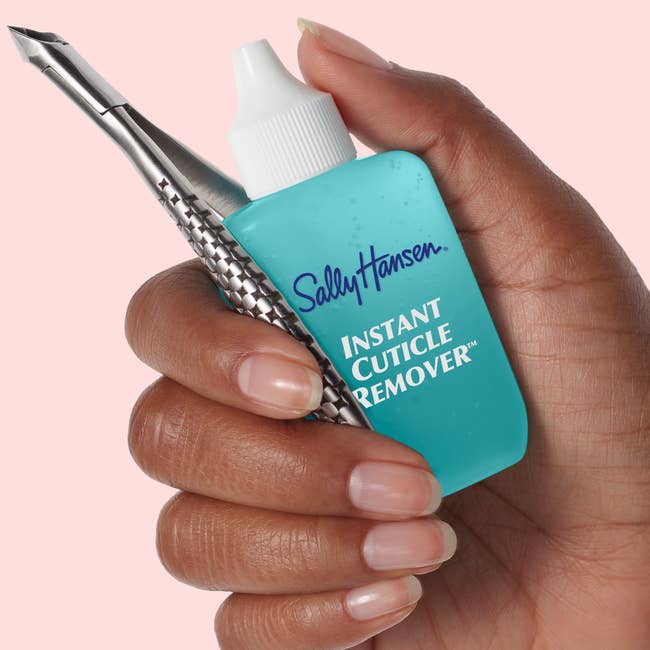 Hand holding Sally Hansen Instant Cuticle Remover vessel  and cuticle tool