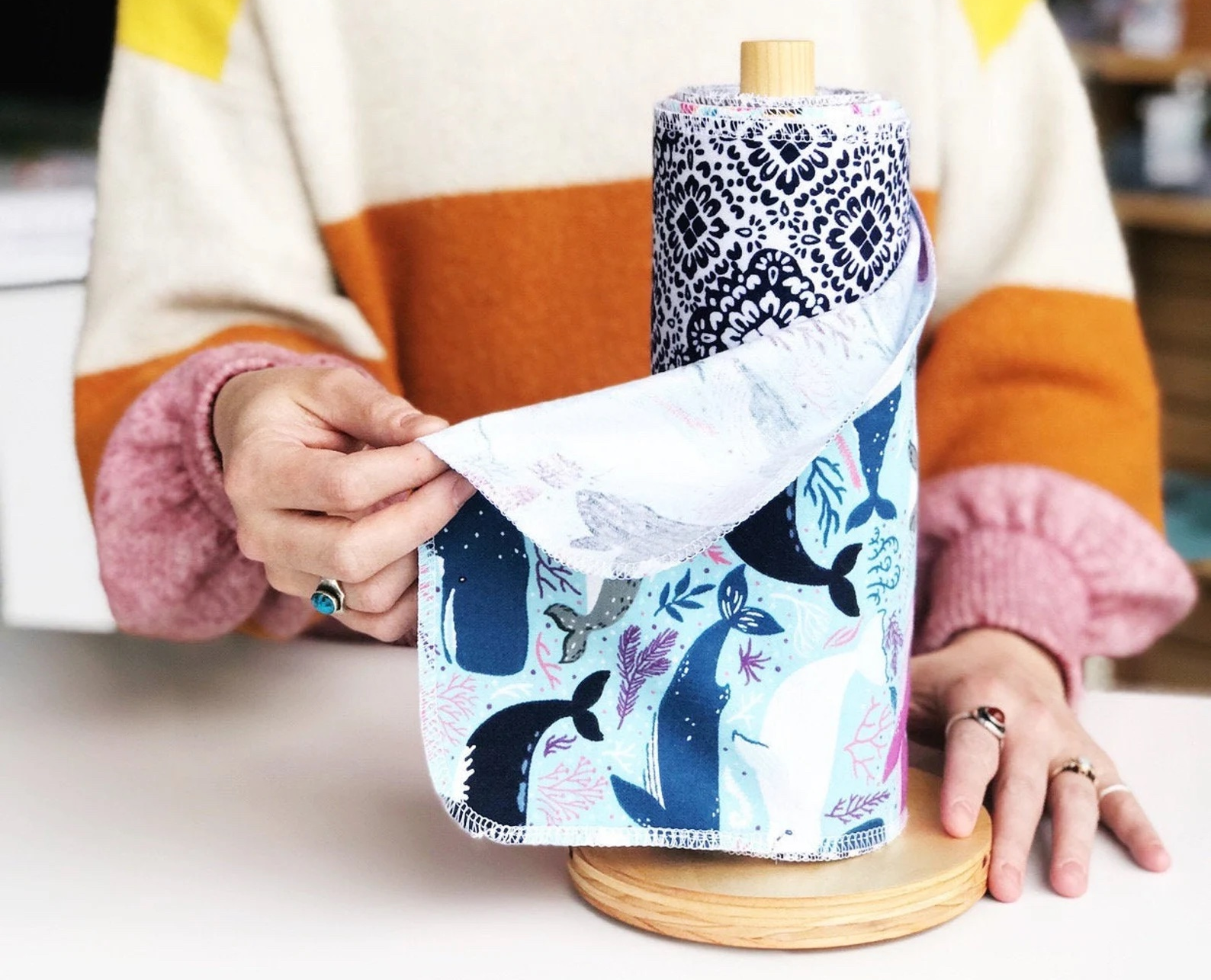 model in a colorful sweater holding a whale-print reusable cleaning towel that's on a wooden roll 