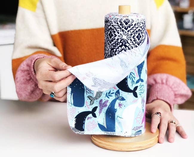 model in a colorful sweater holding a whale-print reusable cleaning towel that's on a wooden roll 