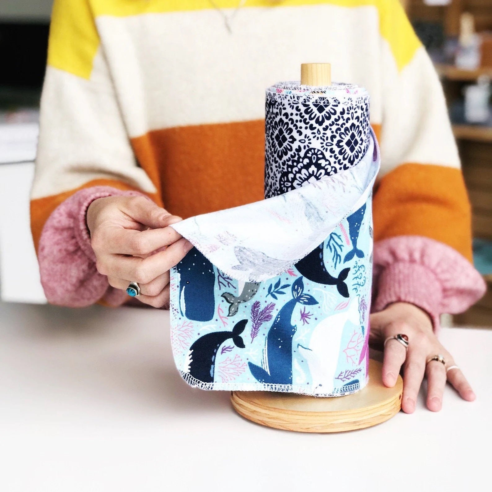 model in a colorful sweater holding a whale-print reusable cleaning towel that's on a wooden roll 