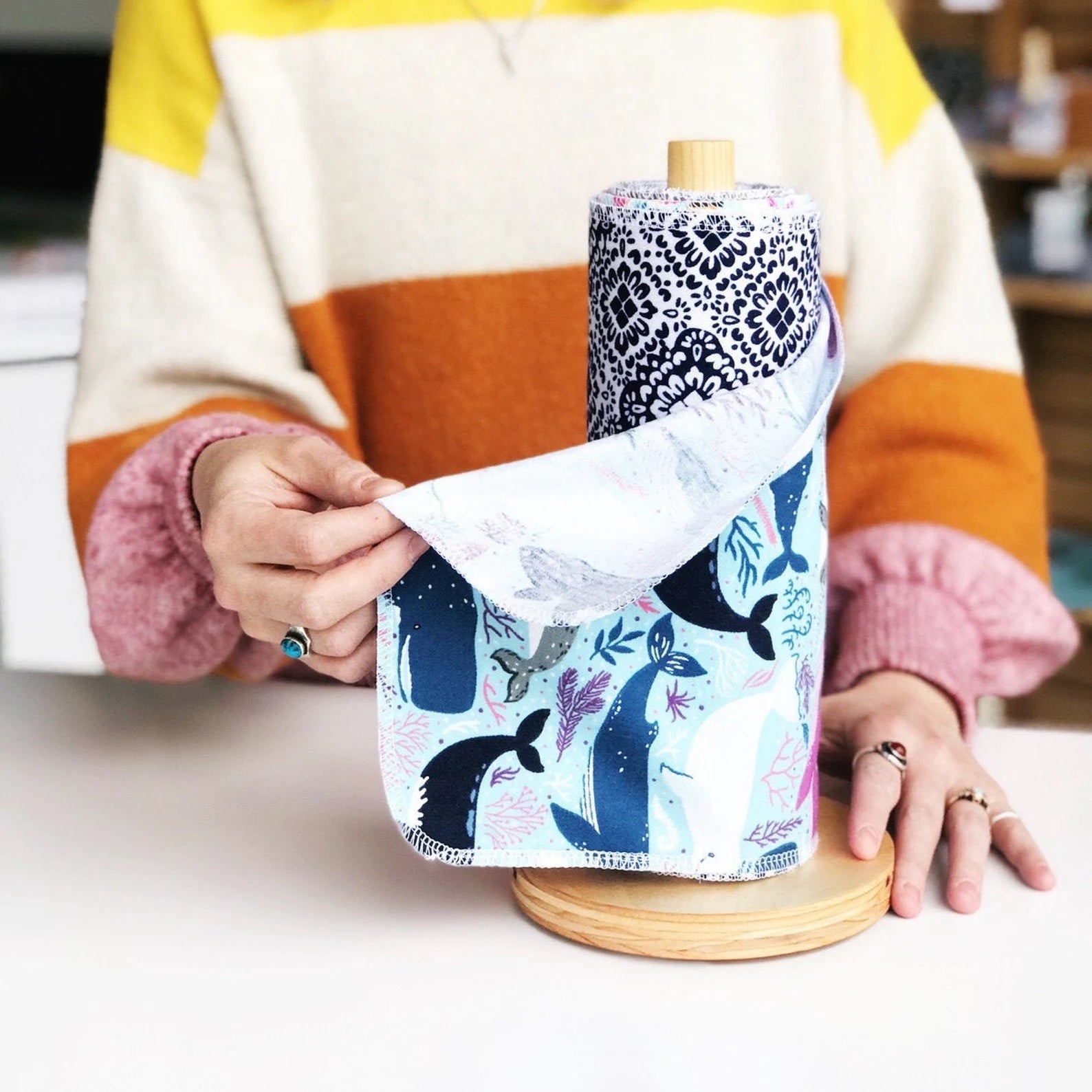 model in a colorful sweater holding a whale-print reusable cleaning towel that's on a wooden roll