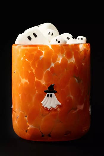 Orange cup with a witch hat-wearing ghost design, filled with marshmallow ghosts featuring cute, small eyes.