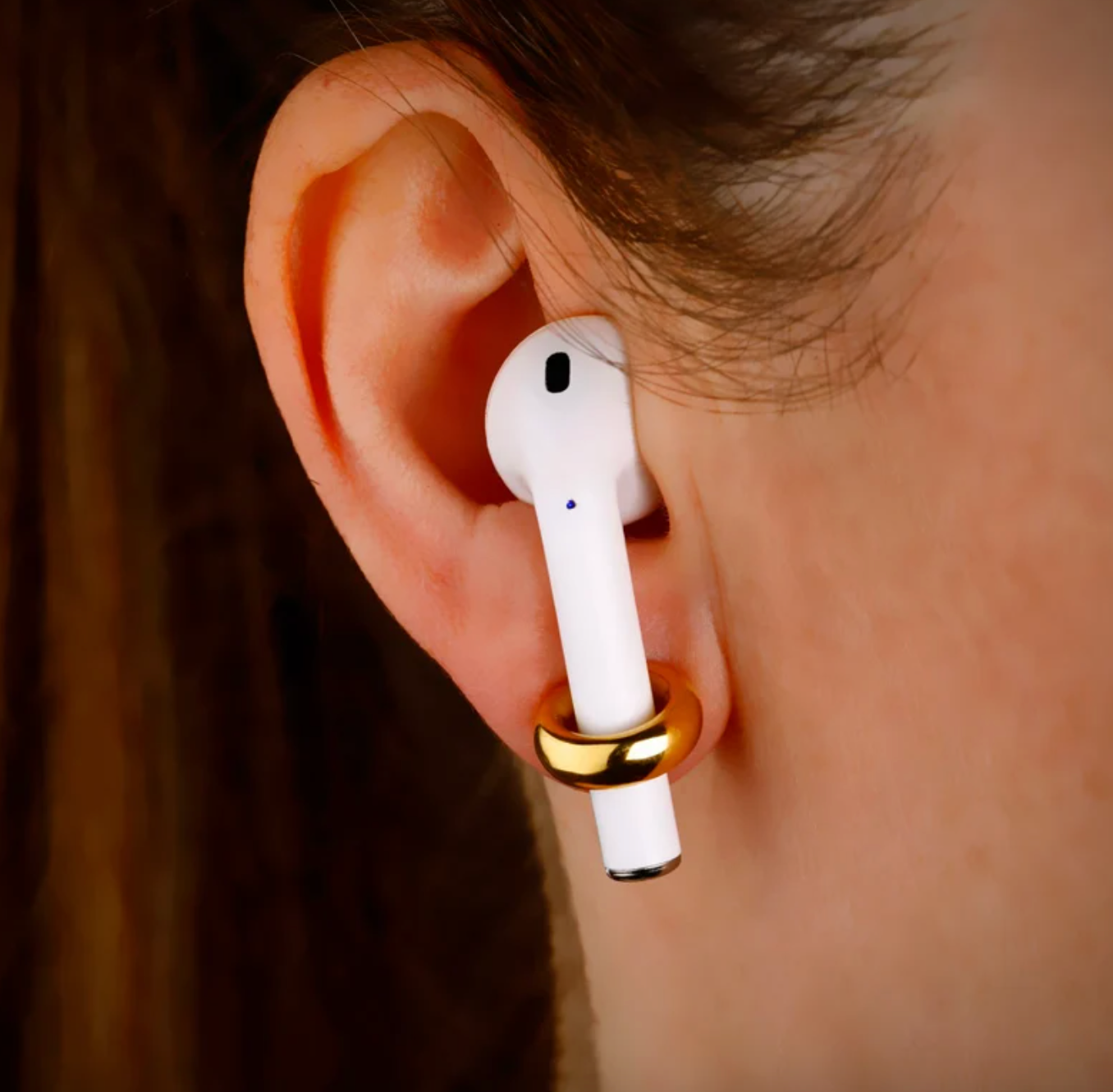 person wearing gold earring that is holding airpod in ear