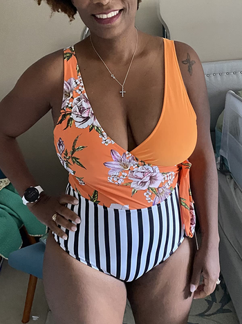 a reviewer wearing a one-piece bathing suit featuring an orange floral top and a black and white striped bottom 