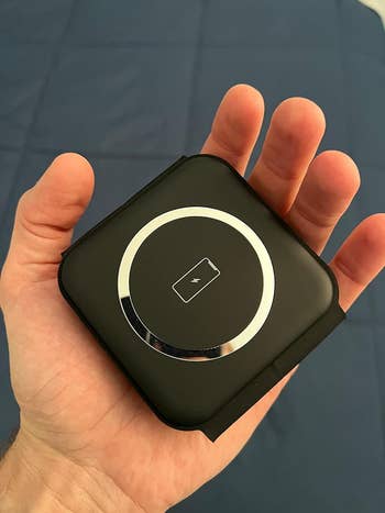 Hand holding a compact, achromatic  wireless charger with a circular charging indicator successful  the center