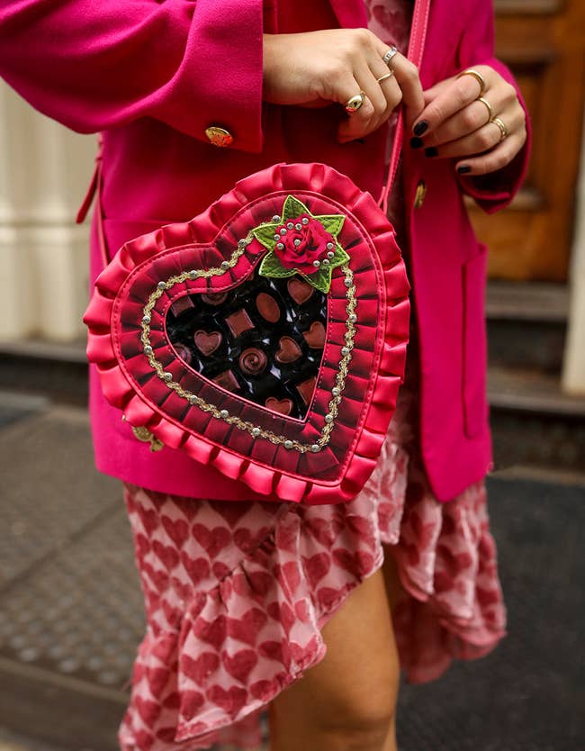 model with crossbody bag shaped like a red frilly heart chocolate box with a clear panel showing fake chocolates