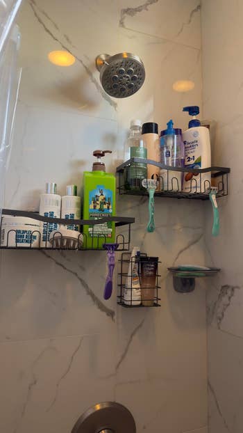 Shower country with marble walls, 2 shelves holding assorted bottles of shampoo, conditioner, assemblage wash, and razors, nether a chrome showerhead
