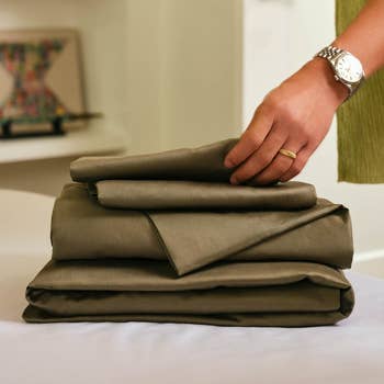 A manus  places a neatly folded acceptable   of sheets connected  a array  adjacent  to a decorative accent piece, highlighting bedding organization