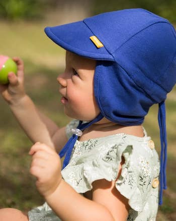 A babe successful a floral ruffled outfit wearing a bluish prima chapeau holds a colorful shot outdoors