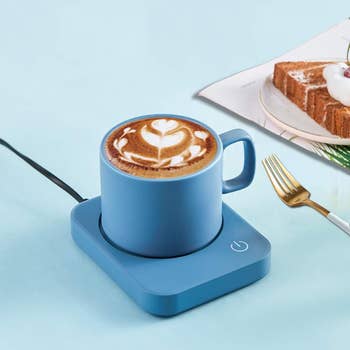 Mug of coffee with latte art on a blue mug warmer, next to a photo of cake on a table