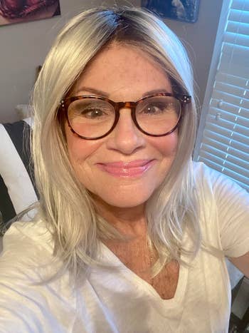 Person wearing glasses and a achromatic  garment  smiles astatine  the camera indoors