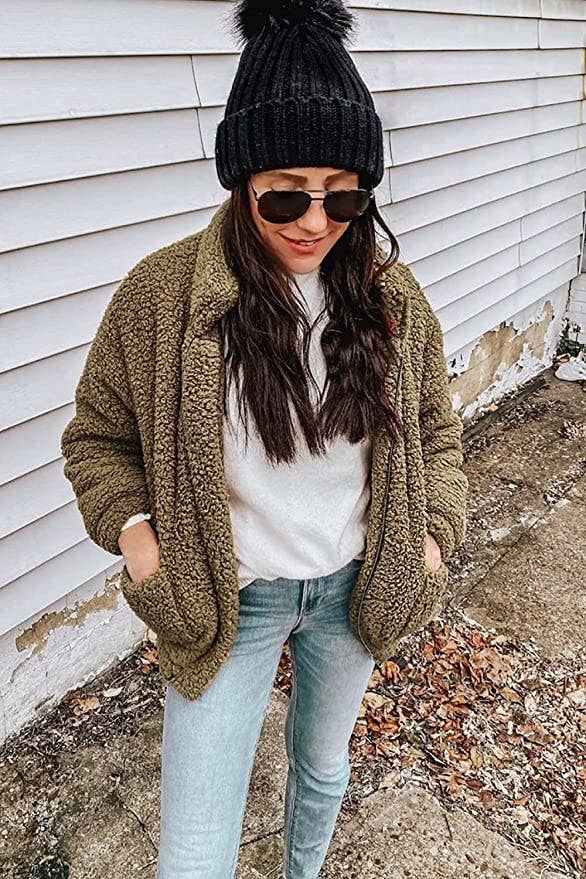 model wearing fluffy green teddy coat with blue jeans, white tee, and a black beanie