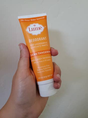 Hand holding a tube of Lume deodorant for underarms and private parts, clean tangerine scent