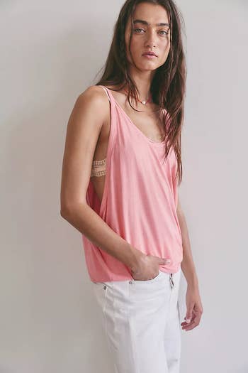Person in a sleeveless, loose-fitting top and light pants, standing against a plain background, showcasing casual, stylish fashion
