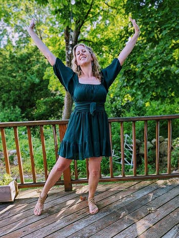 reviewer in a belted short green dress and strappy sandals