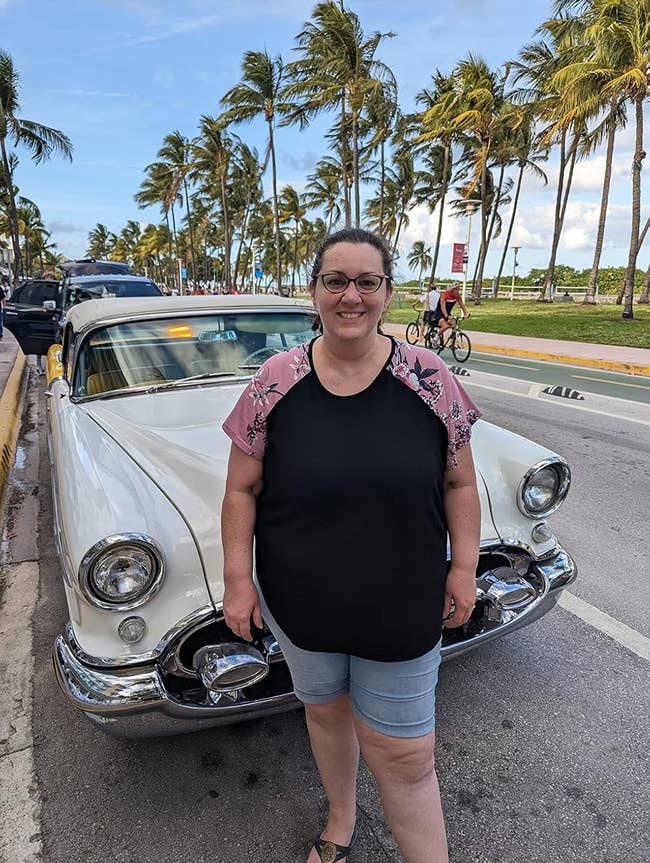 Person lasting  successful  beforehand   of a vintage car   connected  a palm-lined street, wearing a casual floral-sleeved apical  and shorts