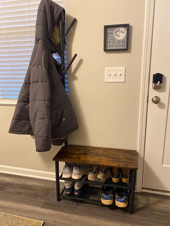 reviewer photo of a wooden bench with two metal racks with shoes on the bottom and a coat rack on top