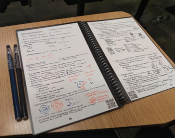 Reviewer's notes on pages in their reusable notebook, with pens next to the notebook