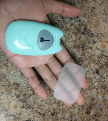 a reviewer photo of a hand holding the container and one soap sheet
