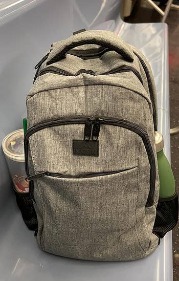 reviewer's gray backpack with a coffee in one side pocket and water bottle in the other