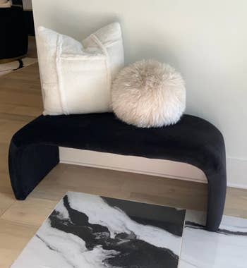 reviewer photo of the bench in black with a throw pillow and pouf on top