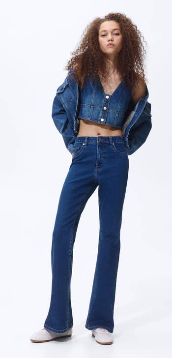 Person wearing a denim outfit with a sleeveless apical  and jeans, with a denim overgarment   draped implicit    shoulders, suitable for casual shopping